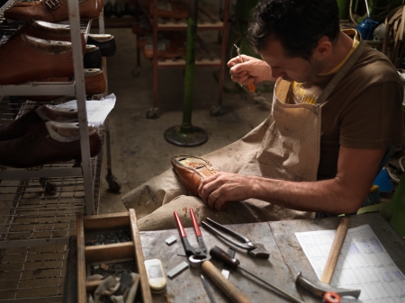 adult man working in a shoe factory, sewing the soles of the shoes manuallyの写真素材
