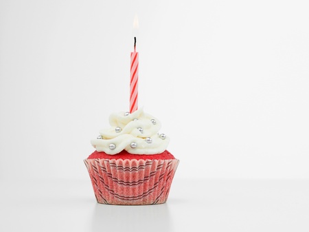 red muffin with cream  white and candy silve one red spiral burning candle on white background isolatedの写真素材
