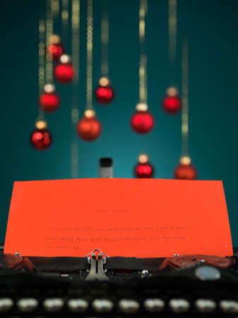closeup of a typewriter with the beginning of a letter to santa written on red paper with red blurred christmas globes on blue backgroundの写真素材