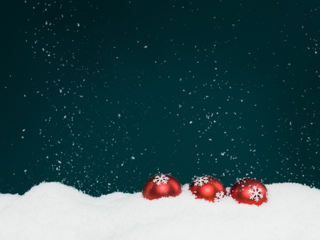 closeup of three red colored christmas globes decorated with glittery snowflakes surrounded with snow, on blue background with falling snowflakesの写真素材