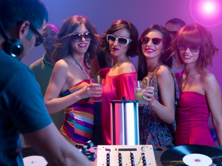 young attractive caucasian girls dancing and having fun at a party with sunglasses and cocktails in their hands in front of a dj mixing music with turntablesの写真素材