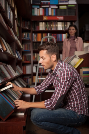 close-up of young caucasian handsome guy in bookstore choosing a book from a lower shelfの写真素材