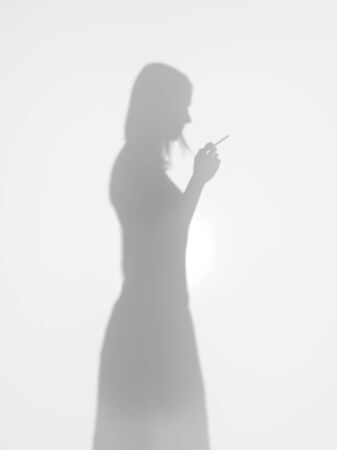 woman silhouette standing with a cigarette in her hand behind a diffuse surface, side view