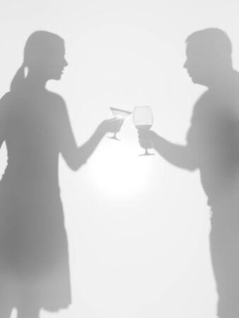 two people silhouettes holding two different glasses, behind a diffuse surface, cheersの写真素材