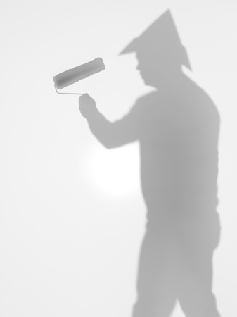 side view of man with paint roller in his hand and a hat  in shape of tringle on his head, behind a diffuse surfaceの写真素材