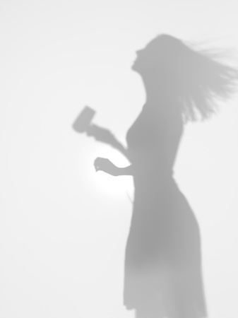 side view of woman drying her hair with a hair drier behind a diffuse surfaceの写真素材