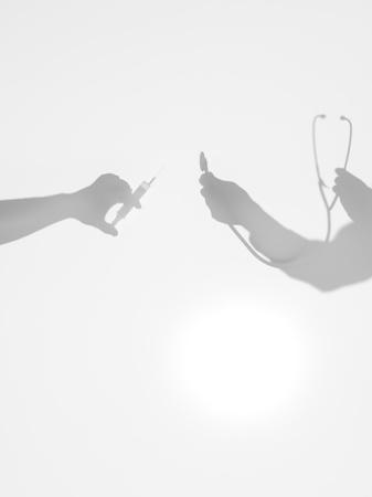 two hands holding a syinge and a stethoscope one in front of the other, behind a diffuse surfaceの写真素材