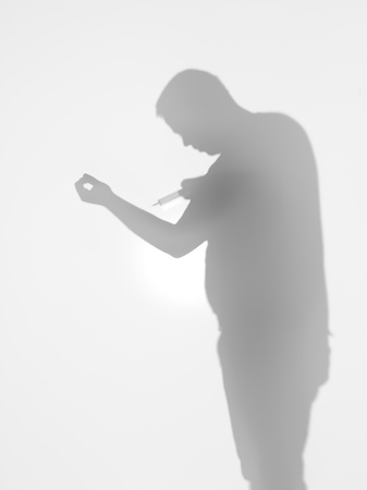 side view of man holding a syringe towards his arm behind a diffuse surfaceの写真素材