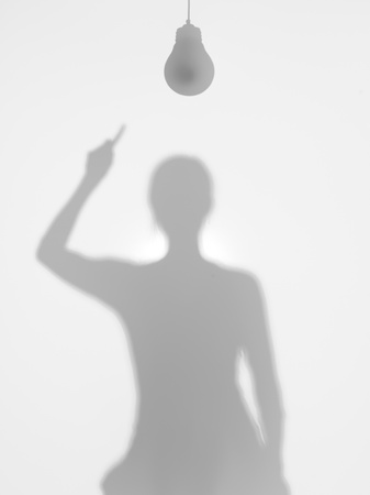 woman with a hanging light bulb on top of her head and pointing towards it with one hand, behind a dffuse surfaceの写真素材