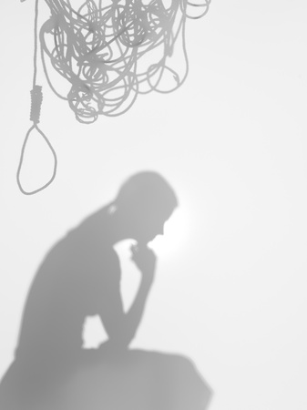 side view of woman sitting in a thinking posture with a tangled hanging rope on top of her head, behind a diffuse surfaceの写真素材