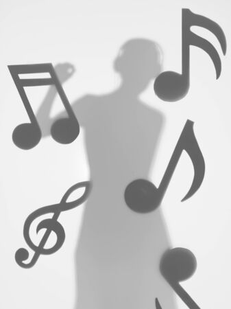 woman dancing and listening to music with headphones, surrounded by musical notes, behind a diffuse surfaceの写真素材