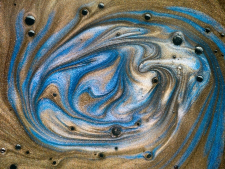 macro of brown and blue pigment mixed with oil with black spots on top of the surfaceの写真素材