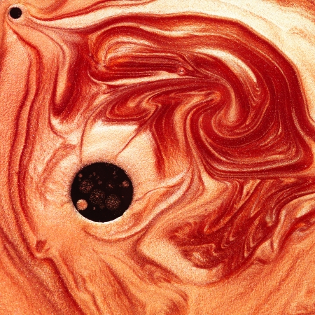 macro of orange and red pigments mixed with oil arranged in a vortex shape with a black spot
