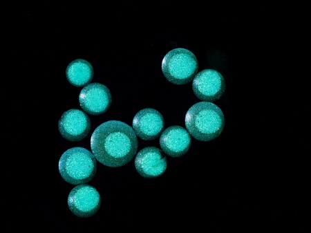 macro of multiple green colored drops of oil in water, on black background