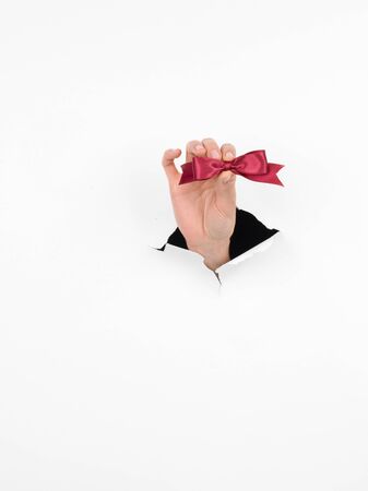 close-up of female hand holding a small burgundy shiny bow through a torn white paper, isolatedの写真素材