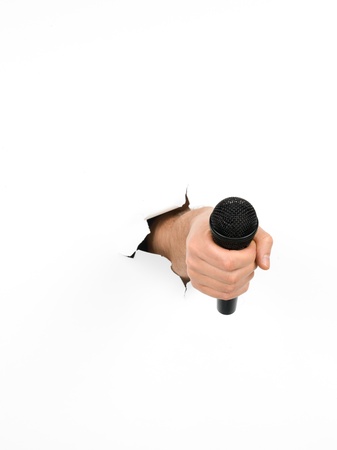 close-up of male hand holding a black microphone through a torn white paper, isolatedの写真素材