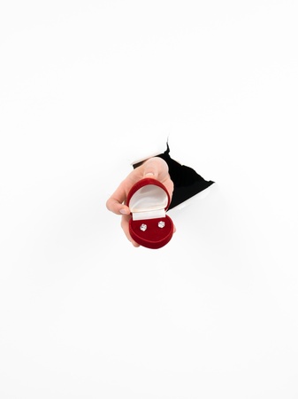 female hand holding a red gift box with earrings inside, through a torn white paper, isolatedの写真素材