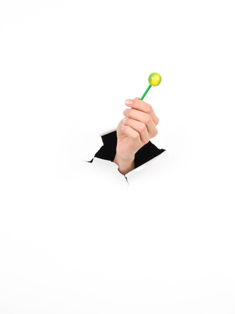close-up of female hand holding a lollipop through a torn white paper, isolatedの写真素材