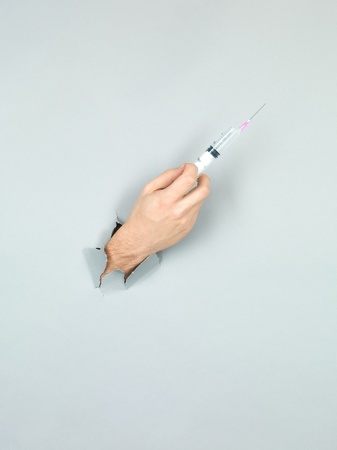 close-up of male hand holding a syringe through a torn grey paper