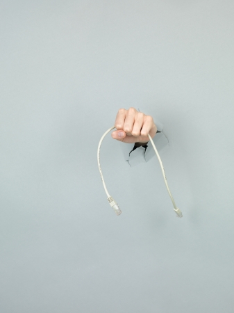 close-up of female hand holding a network cable through a torn grey paperの写真素材