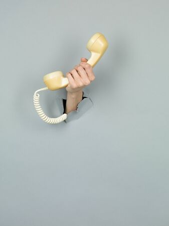 close-up of female hand holding a  yellow telephone through a torn grey paperの写真素材