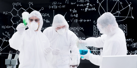close-up of three people conducting a laboratory experiment using laboratory transparent tools and a blackboard with formulas  on the backgroundの写真素材
