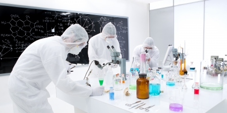 general-view of three people working in a chemistry lab with colorful liquids and transparent tools on a lab table with a blackboard on the backgroundの写真素材