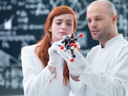 general-view  of a student in a chemistry lab analyzing  a citric acid molecular model holded by her teacher with a blackboard on  the backgroundの写真素材