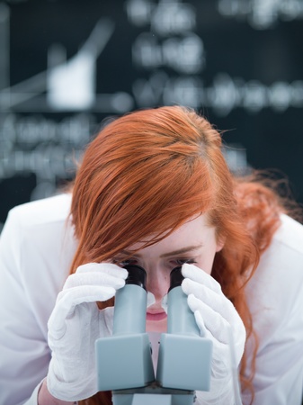 close-up of a student in a chemistry lab analyzing under microscope with a blackboard on the backgroundの写真素材
