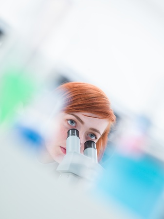 blurred close-up of a student looking in the camera while analyzing under microscopeの写真素材