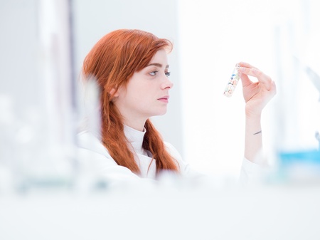 blurred laboratory side-view of a woman analysing pills in a vial