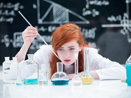 general-view of a student girl conducting a laboratory experiment on a lab table  with colorful liquids and lab tools with a blackboard on the backgroundの写真素材
