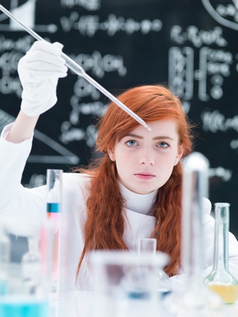 close-up of a student girl conducting a laboratory experiment on a lab table  with colorful liquids and lab tools with a blackboard on the backgroundの写真素材