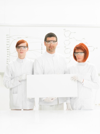 close-up of two beautiful women and a man in a chemistry lab  smiling in the camera with a whiteboard with formulas on the backgroundの写真素材