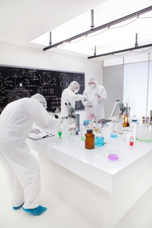 general view  of people working in a chemistry lab around a lab table with colorful liquids and lab tools with a blackboard on the background.の写真素材