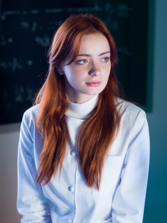 close-up of beautiful redhead female assistant with a blackboard with formulas on backgroundの写真素材
