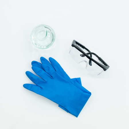 aerial view of a pair of blue lab gloves, protective goggles and an empty bottle on a white tableの写真素材