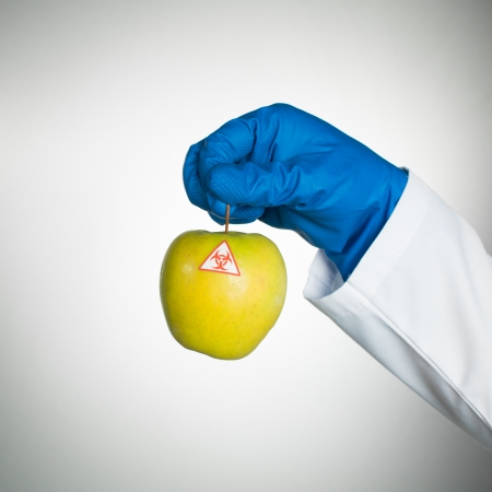 white background with a bio hazardous yellow ripe apple held by a hand in a blue rubber glove and in a lab coatの写真素材