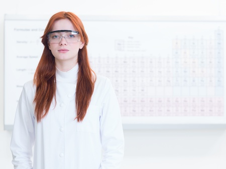 close-up of attractive redhead caucasian girl dressed in a scientist uniform with safety glasses, with periodic table in backgroundの写真素材