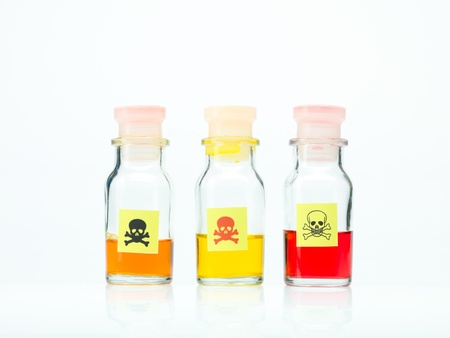 frontal view of three transparent colorless bottles filled with orange, yellow and red liquid and marked as poisonous on a white backgroundの写真素材