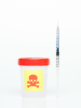 frontal view of a white cup with a red lid, marked as poisonous and an insulin syringe, filled with a transparent liquid againsta a white backgroundの写真素材