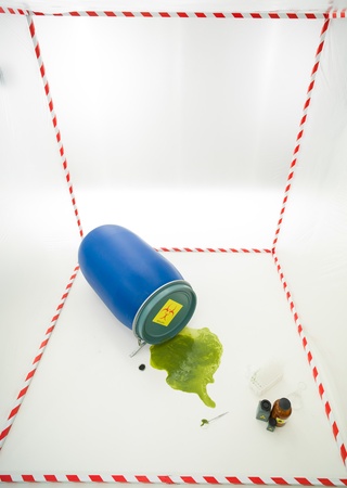upper view of toxic waste spilling from a blue barrel in a white cube surrounded with red and white tapeの写真素材