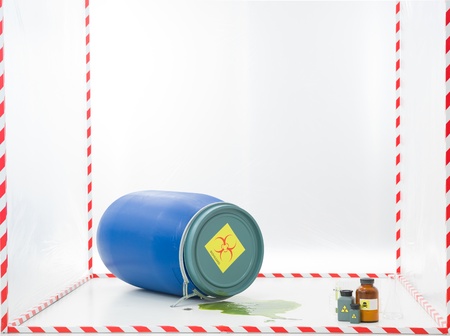 blue barrel with biohazard label and a puddle of green liquid in a cube surrounded with red and white tapeの写真素材