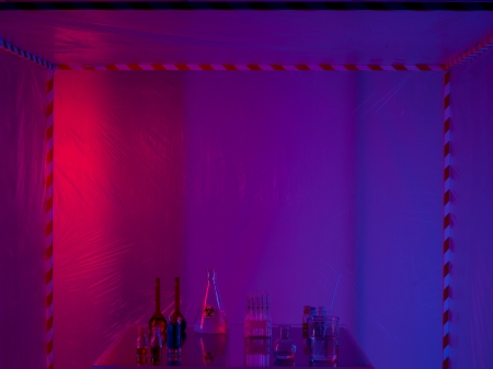 different glass containers filled with differently colored liquids on a glass table in a containment tent, lit by a gradient red, purple and blue lightの写真素材