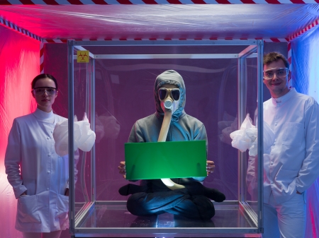 a person inside a protective enclosure, wearing a gas mask, holding a green board with both hands, with two scientists, a man and a woman outside the box, all inside a containment tentの写真素材