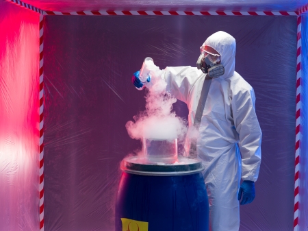 person in a protective suit and gas mask experimenting with steaming substances over a blue plastic...