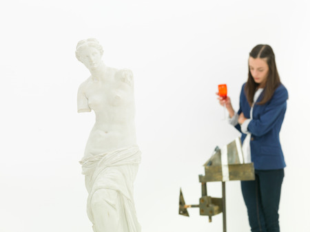 woman scrutinizing sculpture behind a replica of Venus de Milo statue in a museumの写真素材