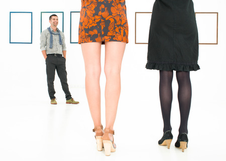 back view of women legs in a white room, standing in front of a man and empty frames on wallsの写真素材