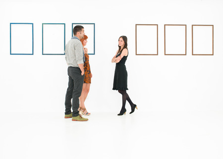 young caucasian people standing in a white room talking, with empty frames displayed on wallsの写真素材