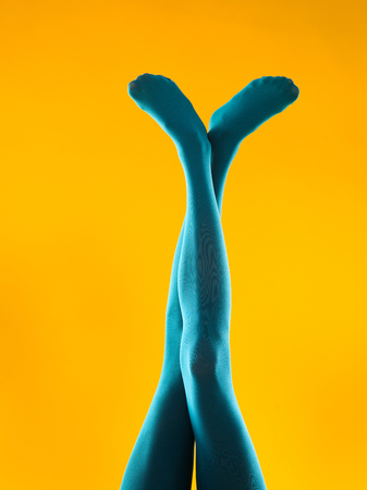 cropped front view of female legs crossed wearing blue pantyhose, on yellow backgroundの写真素材